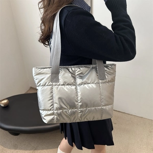 Silver quilted puffer tote bag with metallic finish shown on shoulder in minimalist interior