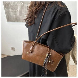 Detail of brown leather tote bag with knot strap, logo embossing and tennis racket charm