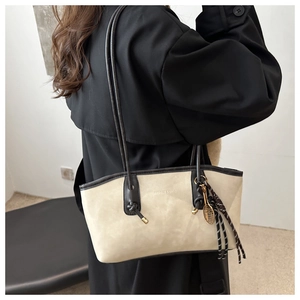 Detail of beige suede tote bag with black straps and decorative tennis racket pendant
