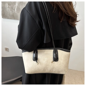 Detail of a beige suede tote bag with black trim worn on shoulder in a minimalist setting