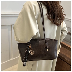 Detail of dark brown tote bag featuring embossed logo and tennis racket charm accessory
