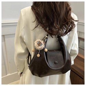 Detail of dark brown crescent shoulder bag with cute plush lion charm and matte finish