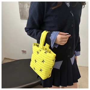 Detail of yellow quilted handbag with black bow embroidery and silver snap button