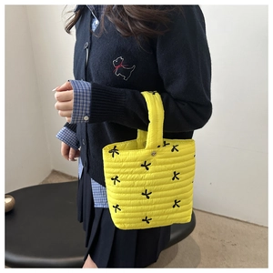 Dettaglio di una borsa tote gialla trapuntata con ricami a fiocco neri in primo piano