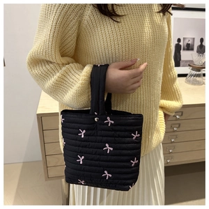Dettaglio di una borsa a secchiello trapuntata nera con ricami a farfalla rosa e imbottitura