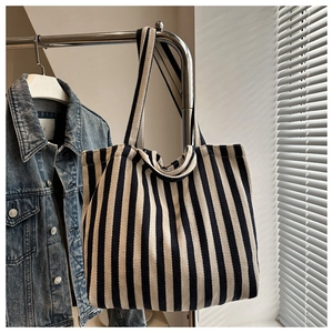 Détail d'un sac cabas en toile à rayures verticales suspendu dans un décor minimaliste