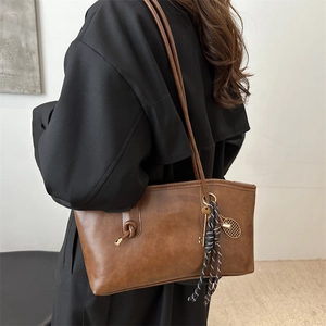 Brown matte leather tote bag with knotted strap and vintage charms on black coat