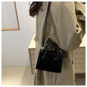Detail of a black quilted mini handbag featuring high-gloss finish and golden hardware