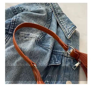 Close-up of brown leather handbag handle with stitching, metal rings, and zip details