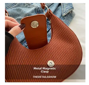 Macro shot showing magnetic snap closure and textured brown leather on crescent bag