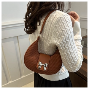 Detail of a brown pleated half-moon shoulder bag with a silver bow buckle on model