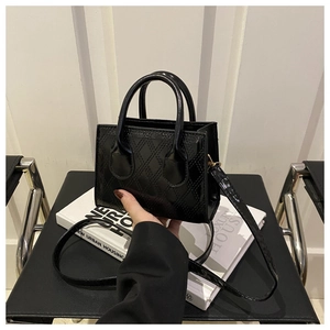 Detail of black glossy handbag with diamond lattice pattern on a white hardcover book