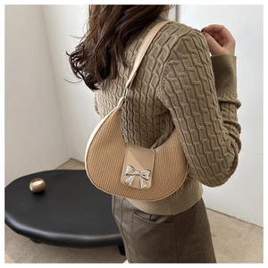 Detail of beige crescent bag with vertical textures and a silver bow buckle on the strap