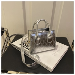 Silver quilted mini tote bag with metallic finish and adjustable shoulder strap on books