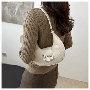 Detailed close-up of white crescent bag featuring a metallic silver bow on textured PU leather