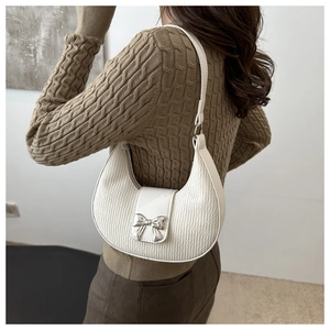 Detail of white pleated crescent bag featuring a silver metal bow buckle on the flap