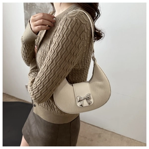 Close-up of off-white crescent bag with silver bow buckle and ribbed texture