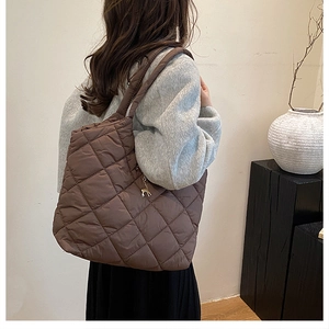 Détail d'un sac cabas en nylon matelassé marron avec un pendentif cerf doré sur la bandoulière