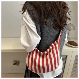 Detail of red and white striped canvas crossbody bag worn by a model in casual setting