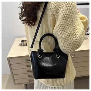 Détail du sac seau en cuir noir brillant avec poignée nouée et anneaux dorés en métal