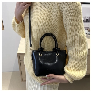 Détail d'un sac seau vintage noir porté avec un pull jaune et une jupe plissée blanche