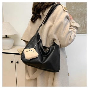 Détail d'un sac cabas en cuir noir avec un porte-clé pain grillé en peluche sur l'épaule