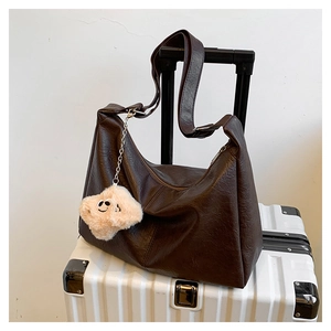 Détail d'un sac cabas en cuir marron foncé avec bandoulière large et pendentif en peluche