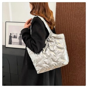 Detail of silver quilted puffer tote bag shown from a side view on a model shoulder