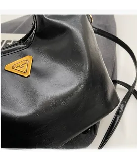 Detail der schwarzen glänzenden Lederbeuteltasche mit goldenem Dreiecksmetall-Logo
