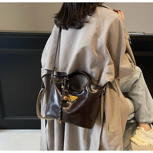 Details der dunkelbraunen Leder-Tragetasche mit Metalldreieck und geflochtenem Anhänger