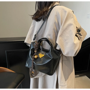 Detailansicht der schwarzen Beuteltasche mit Metall-Logo und dekorativem Taschenanhänger