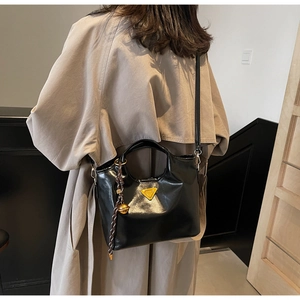 Détail du sac seau noir brillant avec logo jaune et breloque cloche sur un trench-coat