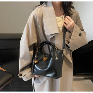 Details der schwarzen Lackleder-Handtasche mit goldenem Logo und Quasten-Anhänger am Mantel