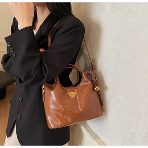 Detail der braunen Vintage-Handtasche aus Leder mit Logo und Glocken-Anhänger am Modell