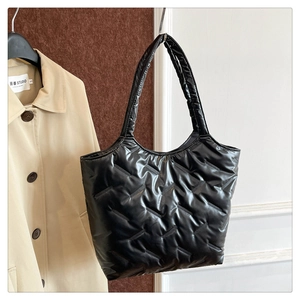 Detail of black quilted puffer tote bag with high-shine finish and padded handles