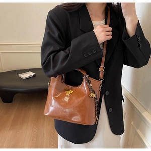 Détail du sac seau marron avec plaque triangle dorée et pendentif clochette tressé