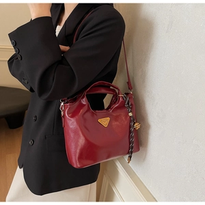 Sac seau en cuir rouge foncé avec logo triangle doré et breloque porté par un mannequin
