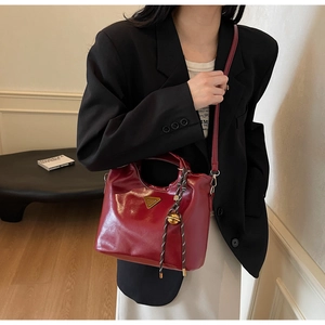 Detail einer burgunderroten Lackleder-Beuteltasche mit Metalldreieck und goldenem Anhänger