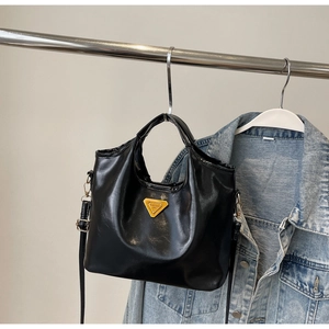 Détail du sac seau en cuir noir brillant avec logo triangulaire doré et boucle