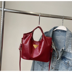 Détail du sac seau en cuir verni rouge avec bijou triangulaire doré et fond en jean