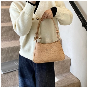 Detail of camel leather baguette bag with lace embossed texture and knot strap accents