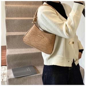 Detailed close-up of beige shoulder bag with floral lace embossed texture and metal trim