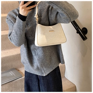 Close-up of beige crescent bag with lace embroidery and gold buckle on grey sweater
