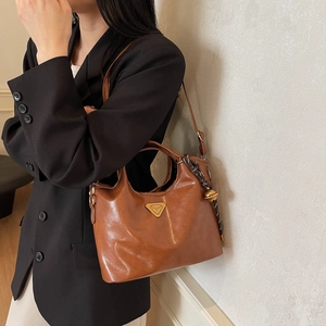 Sac seau marron foncé avec logo métallique et breloque cloche porté sur un tailleur noir
