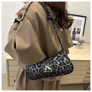 Detail view of leopard print shoulder bag with a gold bow buckle on a trench coat