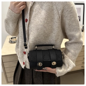 Close-up of black leather crossbody bag with cherry blossom embossing and gold buckles