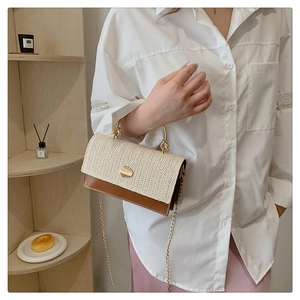 Detail of woven straw and brown leather handbag with gold handle and chain strap