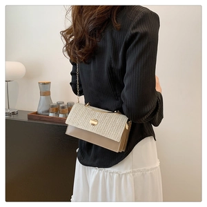 Detail of woven fabric flap handbag with gold metal chain strap on model's shoulder