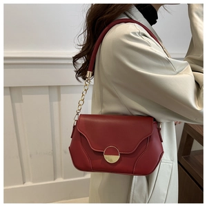 Detail of dark red leather crossbody bag featuring gold buckle and chain strap on model