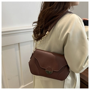 Close-up of brown leather flap bag featuring a gold round buckle and chain strap detail